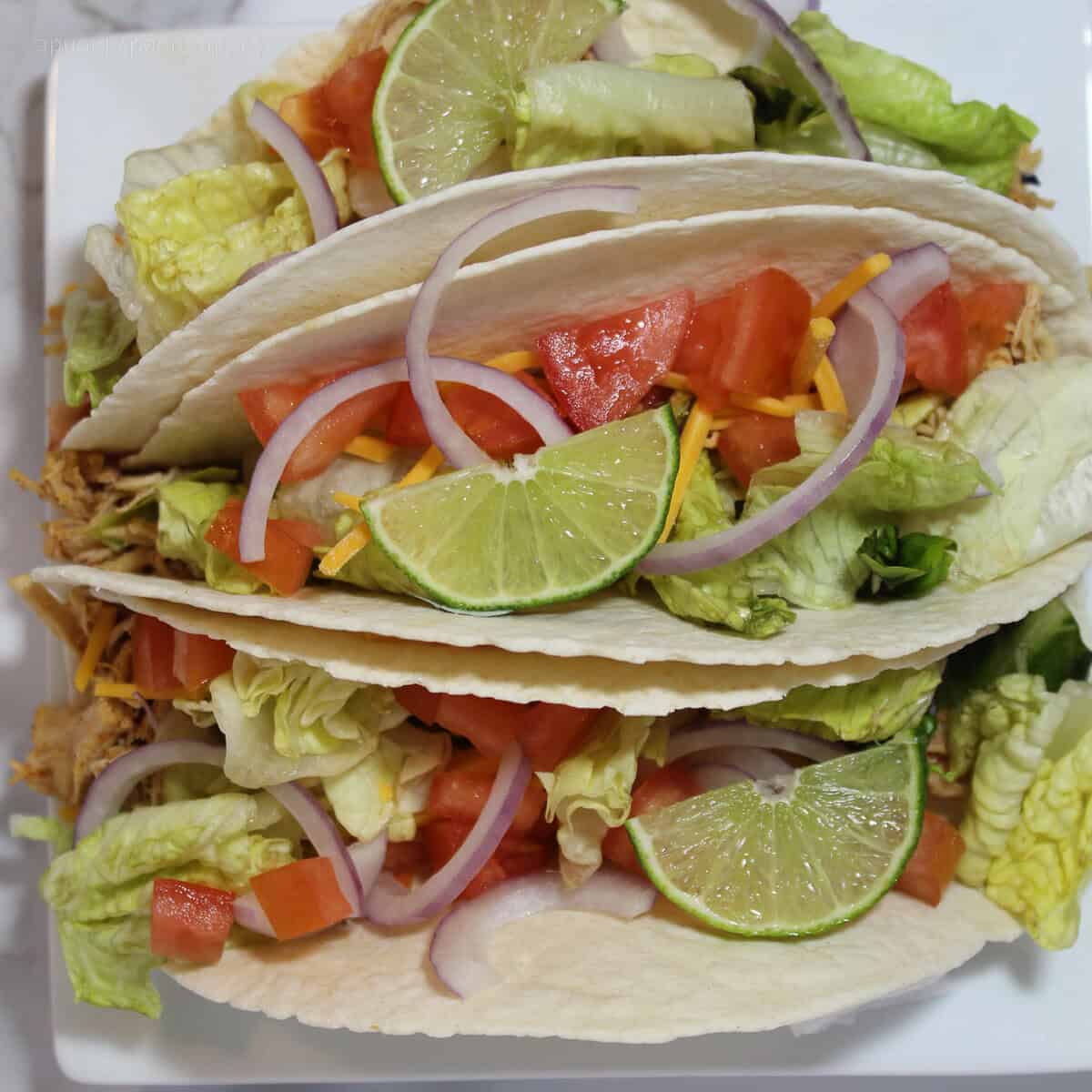 3 Instant Pot Chicken Tacos with toppings on a white plate