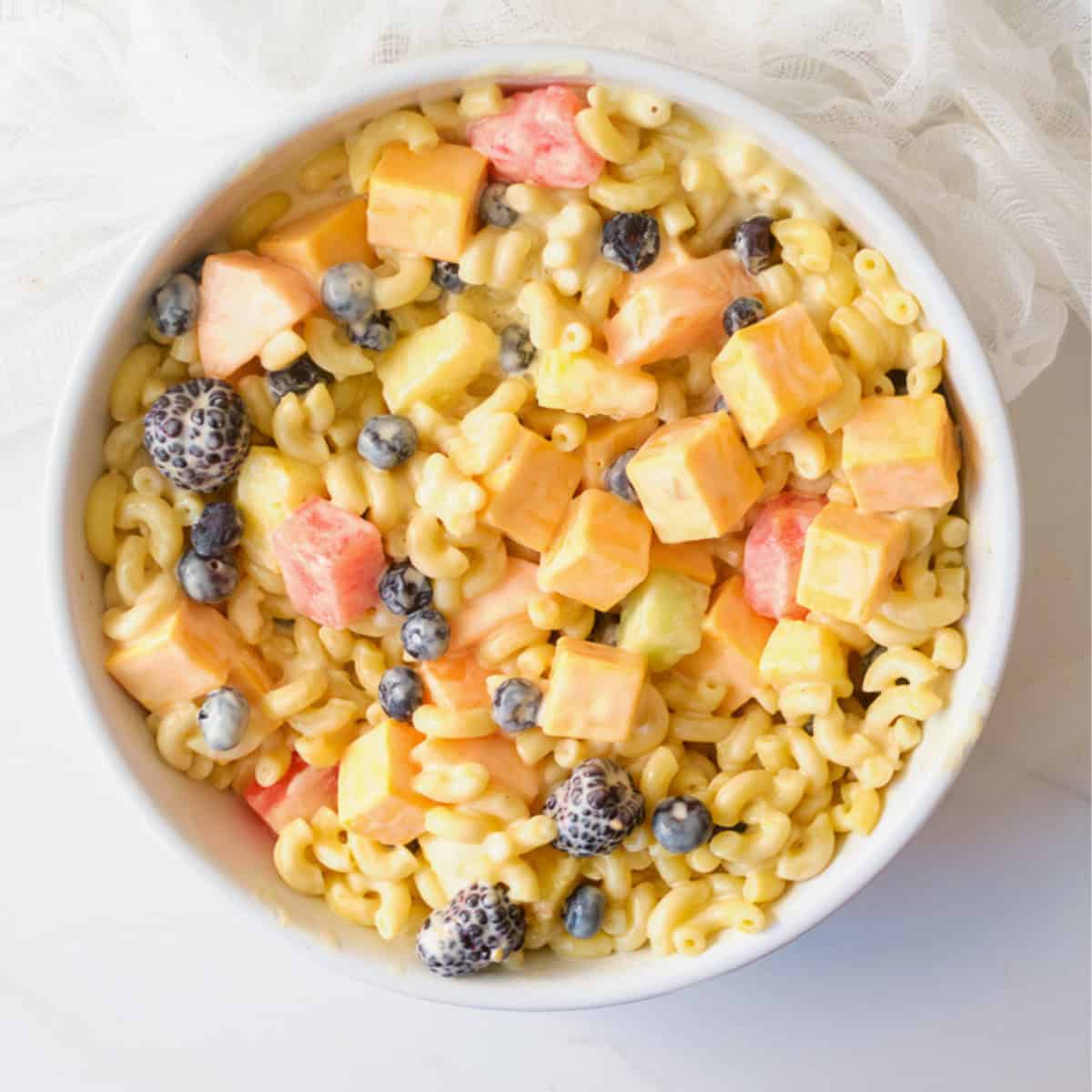 Overhead image of Macaroni fruit salad with berries, cheese, and elbow macaroni in a white bowl on a white background