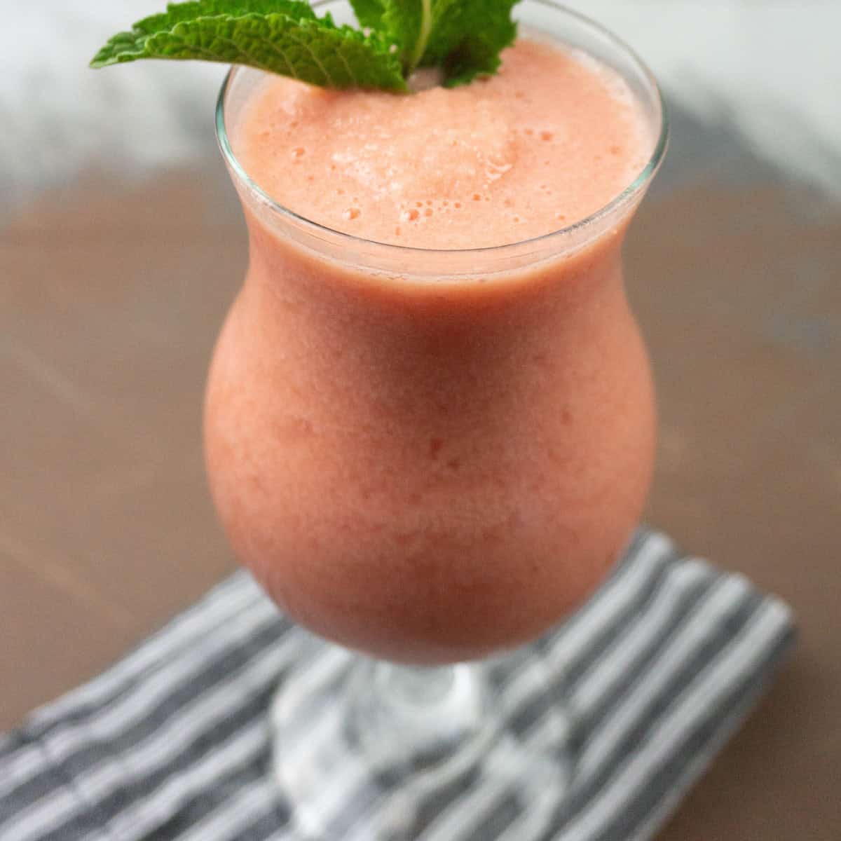 watermelon mint smoothie in a clear hurricane glass garnished iwth fresh mint