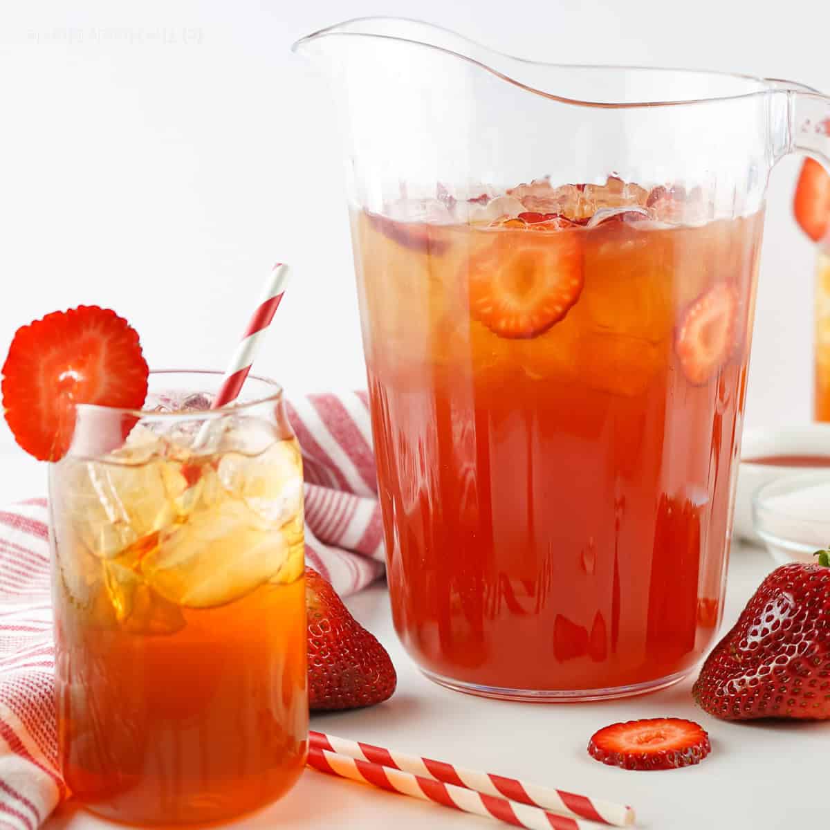 A glass pitcher and a glss of strawberry sweet tea made with fresh strawberries