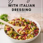 3 Bean Salad With Italian Dressing Title Graphic for Pinterest featuring a white bowl with salad and a wooden spoon on a beige background